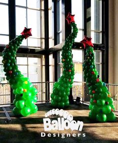 three christmas trees made out of balloons in front of windows with the words balloon designers written on them