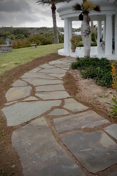 a stone path leading to a white house with palm trees in the backgroud