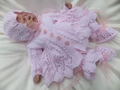 a baby doll laying on top of a white bed covered in pink crochet