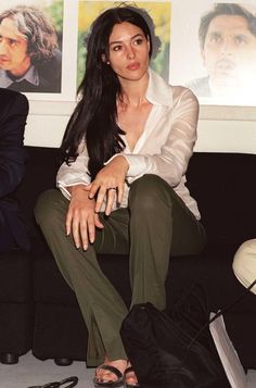 a woman sitting on top of a black couch next to a bag and shoes in front of pictures