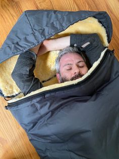 a man laying on the floor in a sleeping bag with his head tucked under it