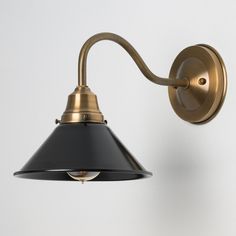 a black and gold light fixture on a white wall with a gray shade hanging from it's arm