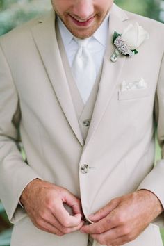 a man in a white suit and flower boutonniere adjusts his bow tie