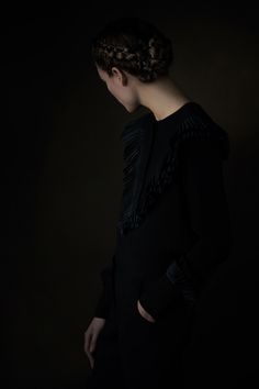 a woman standing in the dark with her back turned to the camera, wearing a black dress