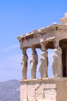 some statues on the side of a building with mountains in the backgrouds