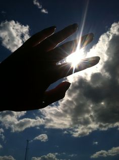 a person's hand reaching up into the sky with clouds in the back ground