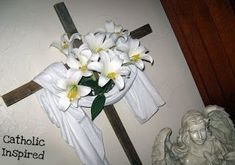 a cross with flowers on it next to an angel statue and a wall decoration that says, catholic inspired