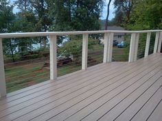 a wooden deck with white railing and cars parked on the other side, in front of some trees