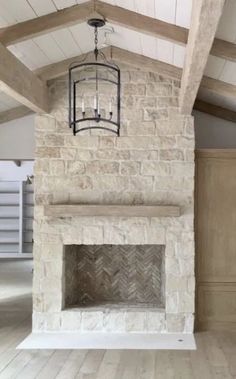 an empty room with a stone fireplace and wood flooring on the walls, along with a chandelier hanging from the ceiling