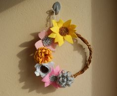 a wreath made out of paper flowers and pineconis hangs on a beige wall