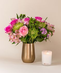 a vase filled with pink flowers next to a lit candle