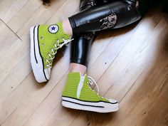 a woman in black leggings and neon green converse sneakers sitting on the floor