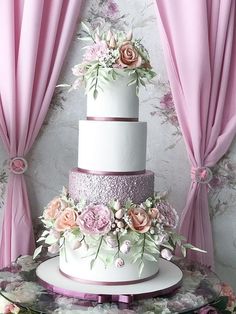 a three tiered wedding cake with pink flowers on top and purple curtains behind it