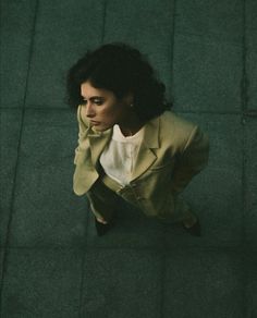 a woman is sitting on the ground looking down at her cell phone and wearing a jacket