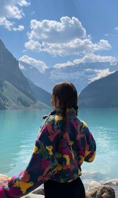 a woman sitting on rocks looking out over the water at mountains and clouds in the sky