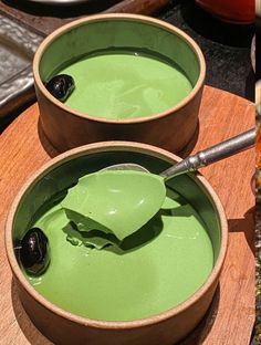 two bowls filled with green liquid on top of a wooden table