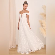 a woman in a white wedding dress standing on a wooden floor next to a plant