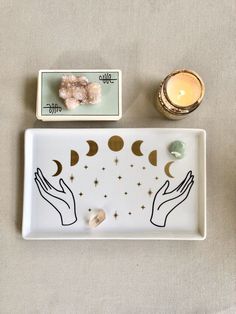 a plate with two hands holding the moon on it next to a candle and some other items