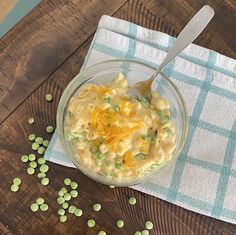 a bowl of macaroni and cheese sits on a table with peas scattered around it