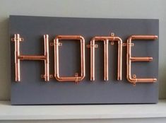 the word home made out of copper pipes on a gray background with white shelves in front of it