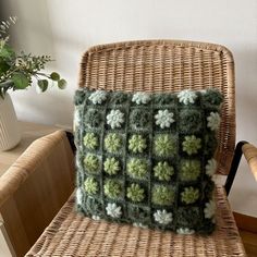 a green and white crocheted pillow sitting on top of a wicker chair