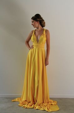 a woman in a long yellow dress standing against a wall with her hands on her hips