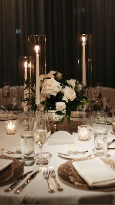 the table is set with silverware and white flowers in glass vases, along with candles