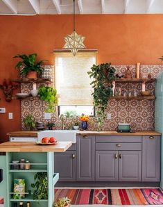 a kitchen with orange walls and grey cabinets, an island in front of the sink