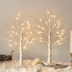 three white birch trees with lights in them on a fur covered table next to a lit candle