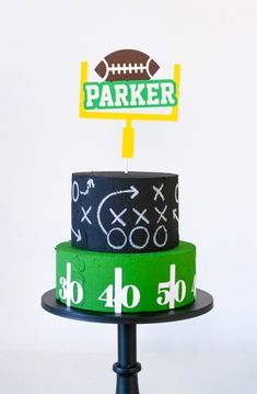 a three tiered cake decorated with footballs and the words parker on top, sitting on a black stand