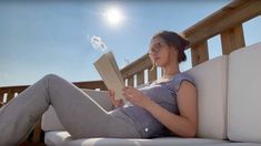 a pregnant woman reading a book while sitting on a white couch in front of the sun