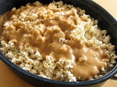 a bowl filled with popcorn covered in gravy on top of a wooden table