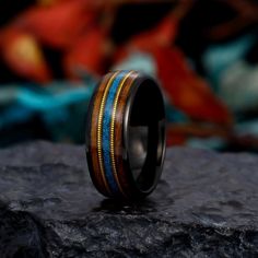 a black ring with gold and blue inlays sitting on top of a rock