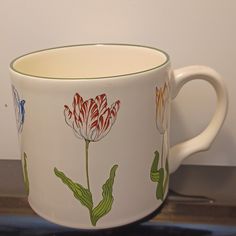 a white coffee cup with flowers painted on the side and green trim around the edge