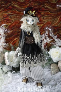 a white and black doll is standing in the snow with flowers behind it, wearing a hat