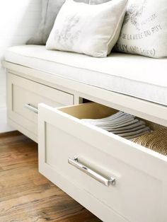 a white bench with two drawers and plates in the bottom drawer next to some pillows