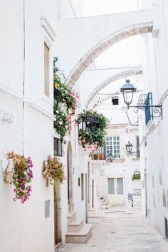 an alley way with flowers hanging from the buildings