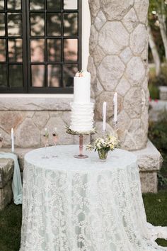 a white wedding cake sitting on top of a table next to a stone wall and windows