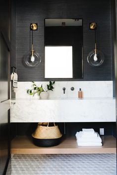 a bathroom with black walls and marble counter tops, two lights above the sink and a mirror on the wall