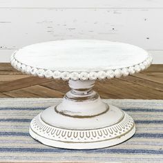 a white cake plate sitting on top of a blue and white striped tablecloth next to a wooden wall