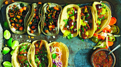 several tacos are lined up on a tray next to salsa and lime wedges