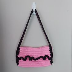 a crocheted pink purse hanging from a hook on a white wall with black trim