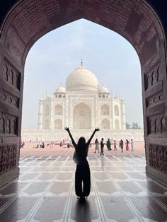 a woman is standing in front of the taj - i, with her arms up