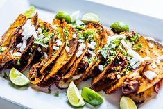 a white plate topped with lots of tacos and limes on top of it