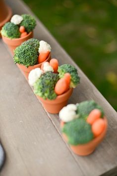 carrots and broccoli are arranged in small pots on a wooden table outside