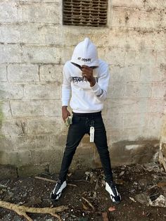 a young man wearing a white hoodie and black pants standing in front of a brick wall