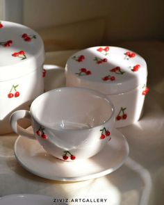 three white cups and saucers with red cherries on them sitting on a table