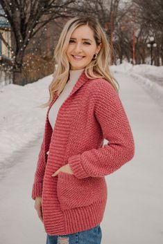 a woman standing in the snow wearing a red cardigan sweater and jeans with her hands on her hips