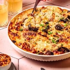 a casserole dish with cheese and vegetables in it on a table next to two glasses of orange juice