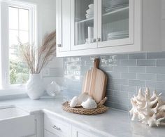 a kitchen with white cabinets and gray tile backsplash, sea shells and utensils on the counter